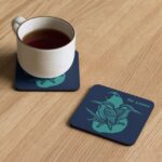 A white mug of tea placed on the heat-resistant Midnight Kingfisher Coaster on a wooden table.